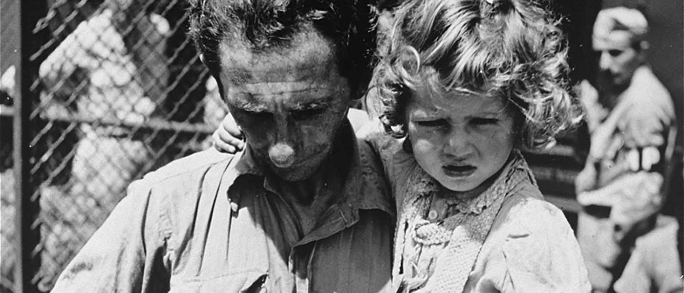 フォート・オンタリオ難民避難所の受付時に自身のタグをチェックする父親と父親に抱かれた娘
