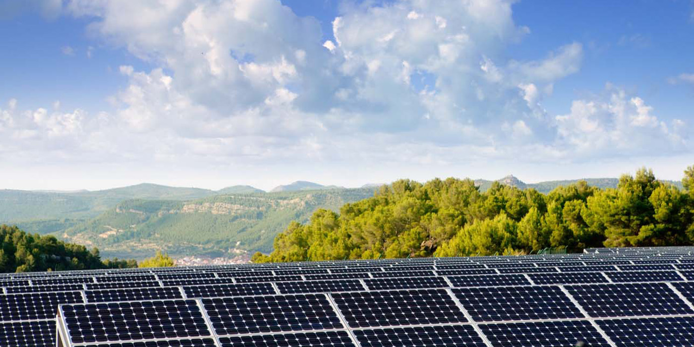 Solar panels in the foreground overlooking a village in a green valley with blue sky.