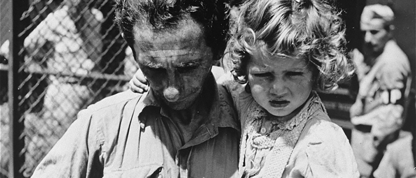 A father, holding his daughter, checks his tags during check in at the Fort Ontario refugee shelter.